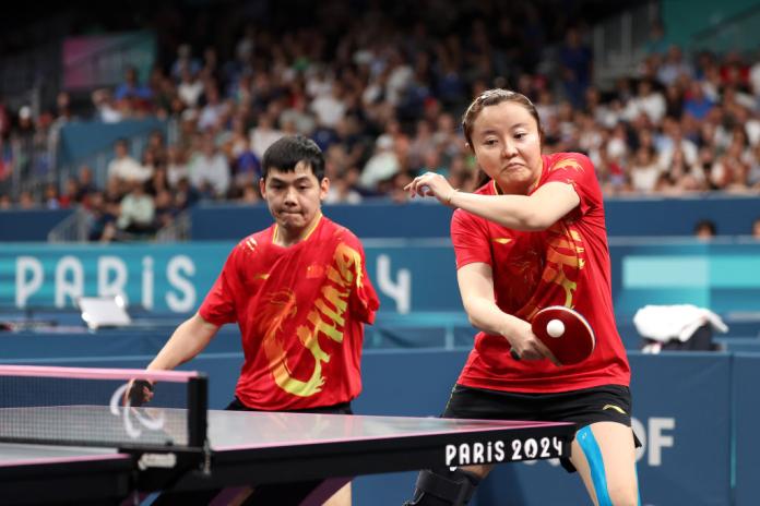 A female Photo shows a mixed doubles Para table tennis match - a female player returns a shot next to her male doubles partner